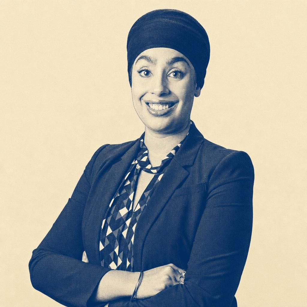 Mohnaam Kaur Shergill, in a black head covering and blazer over a patterned blouse, arms crossed, photographed smiling.